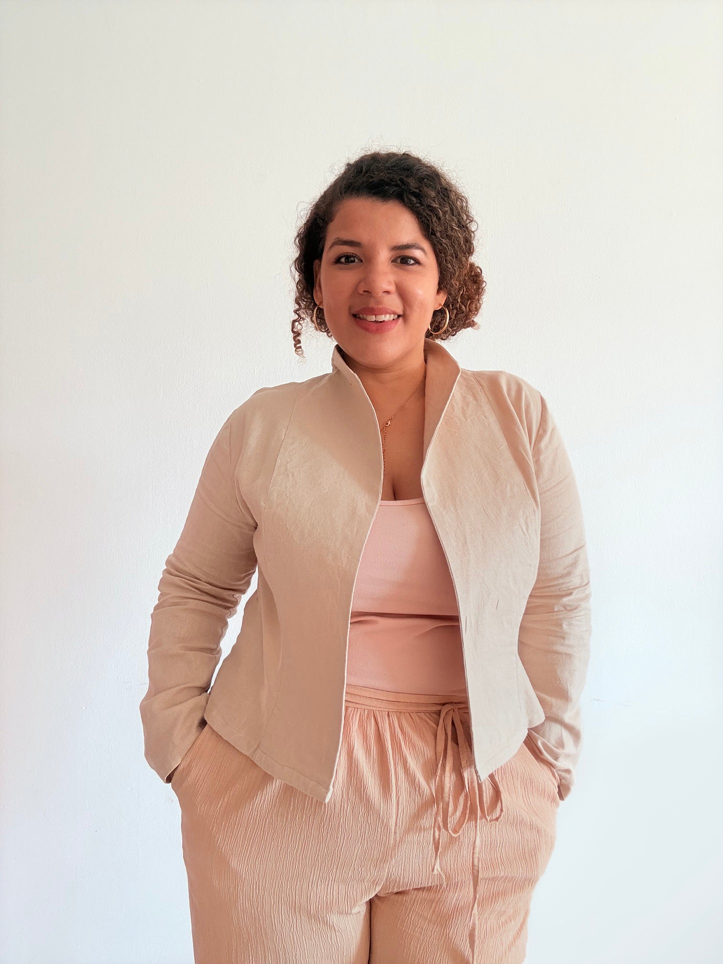 Woman wearing a beige camelia unlined jacket over a pink top and pants on a white background
