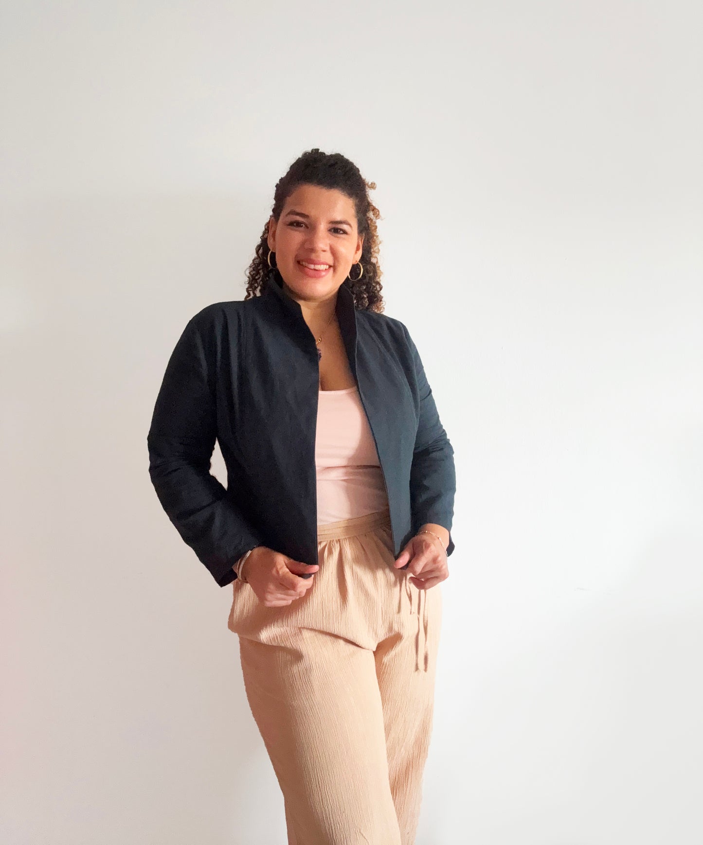 Woman wearing a black jacket and beige pants against a white background