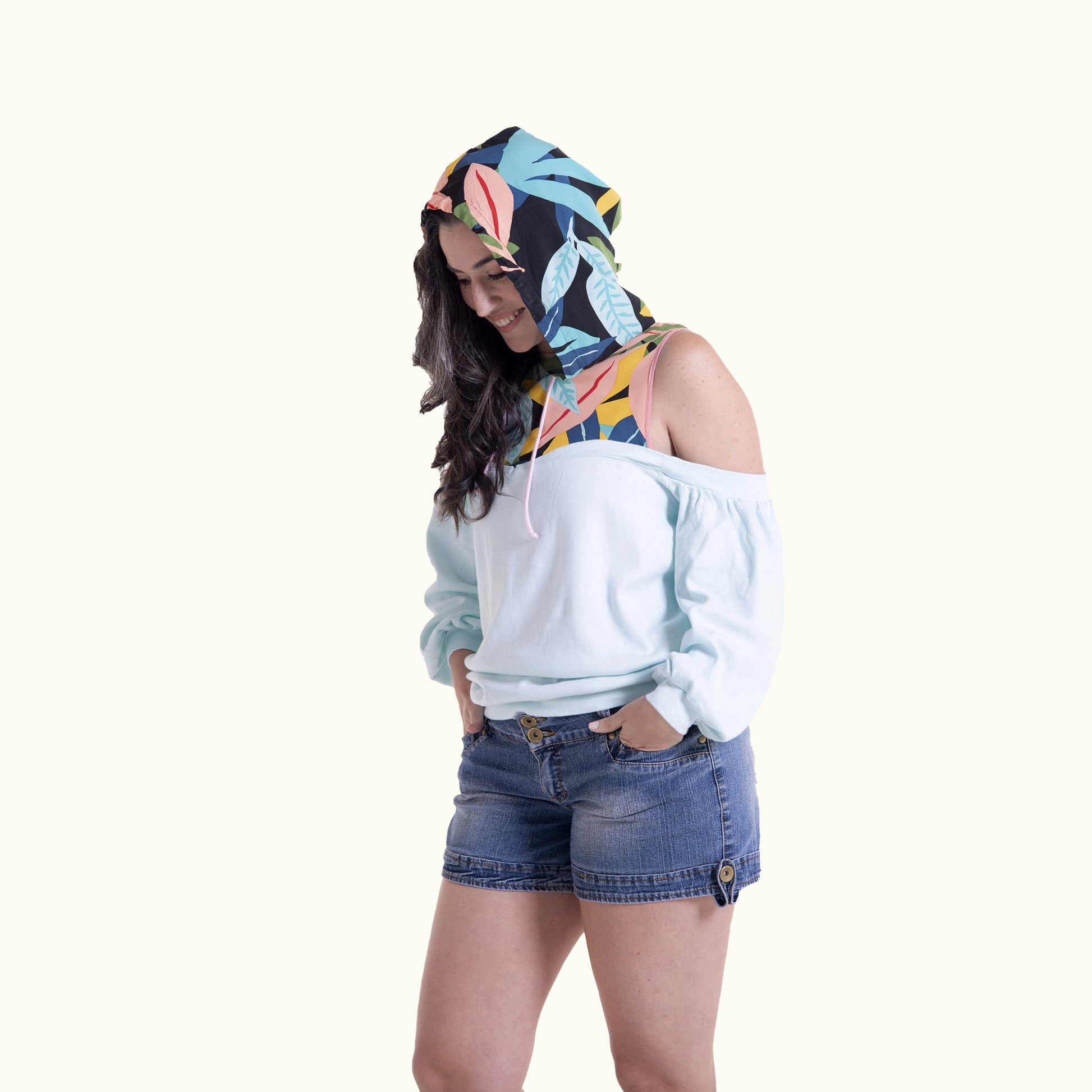 Woman wearing a colorful hooded sweatshirt and denim shorts on a white background
